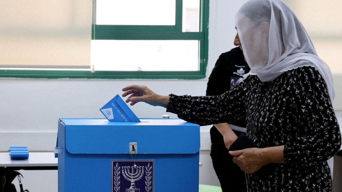 Woman in a headscarf puts ballot paper into box